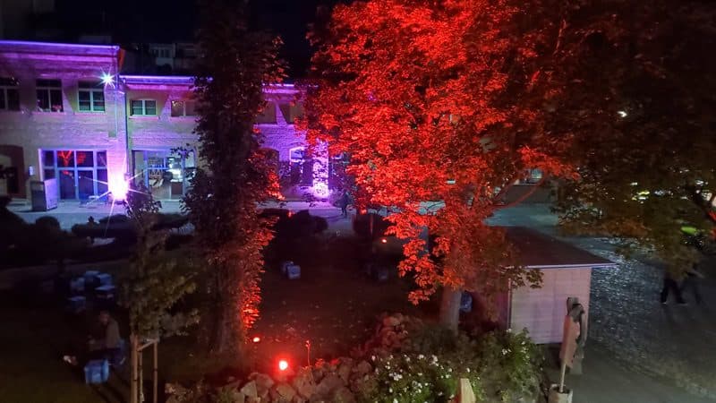 Der Innenhof des MONOPOL Leipzig bei Nacht, farbig angestrahlte Bäume und Fassaden