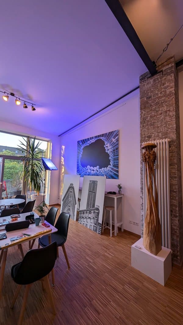 Galerieraum mit Fotografien, Holzskulptur und Tischen